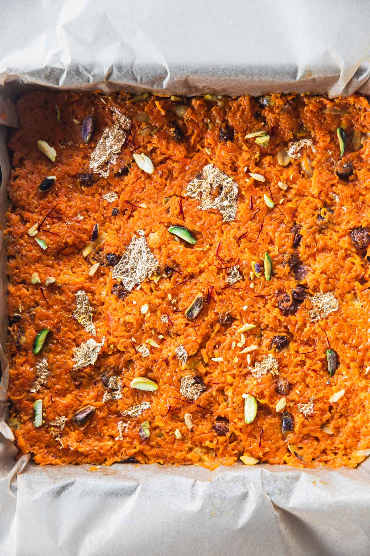Gajar ka halwa (Carrot Halwa or Indian Carrot Pudding) set in a baking sheet and decorated with edible gold foil and slivered nuts.