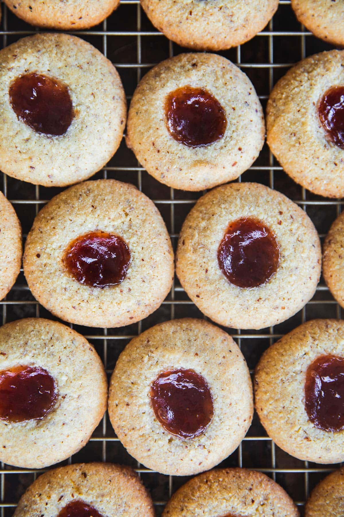 Baked Frangipane Jam Drops lined up on a wire rack, strawberry jam glistening in pools on each biscuit.