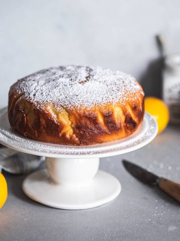 Easy lemon cake, golden and dusted with icing sugar on a cake stand.