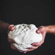 Easy Pizza Dough held in two hands against a dark backdrop.