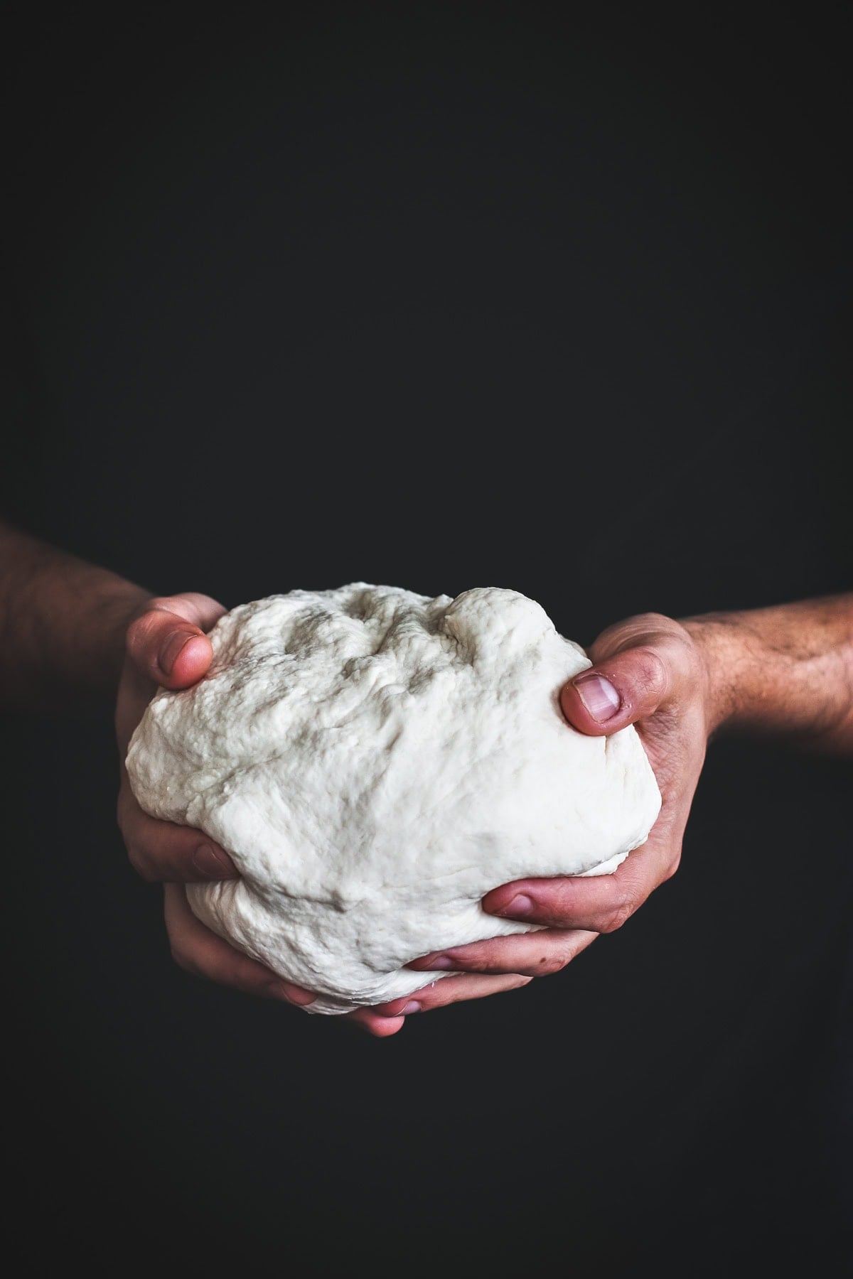 Easy Pizza Dough held in two hands against a dark backdrop.