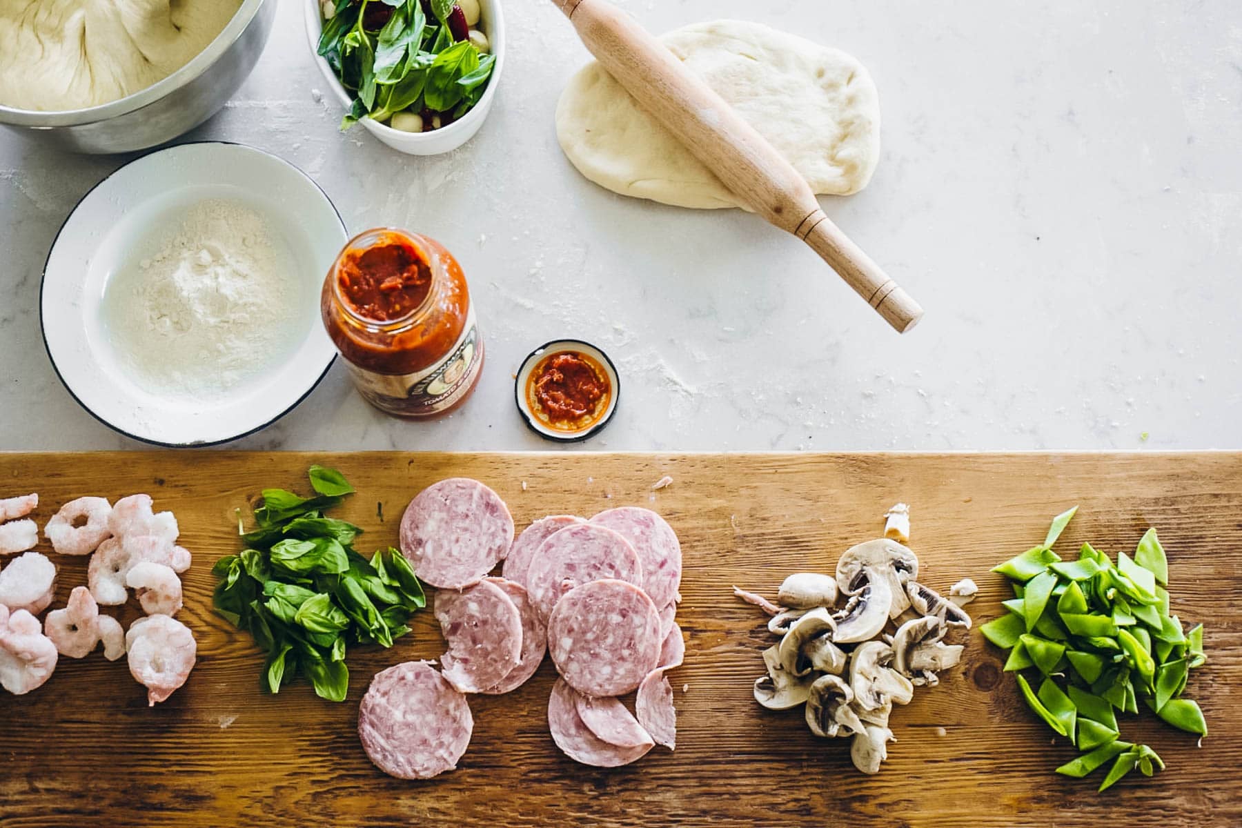 Rolling the pizza dough into desired shape using a rolling pin.