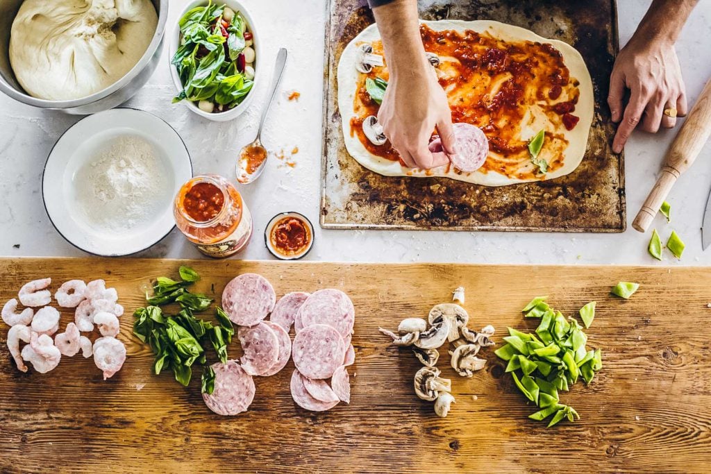 Topping rolled pizza dough with pizza sauce and toppings.
