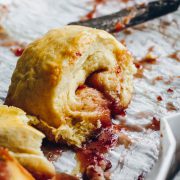 A sticky pinwheel jam scone on a tray with strawberry jam oozing out.