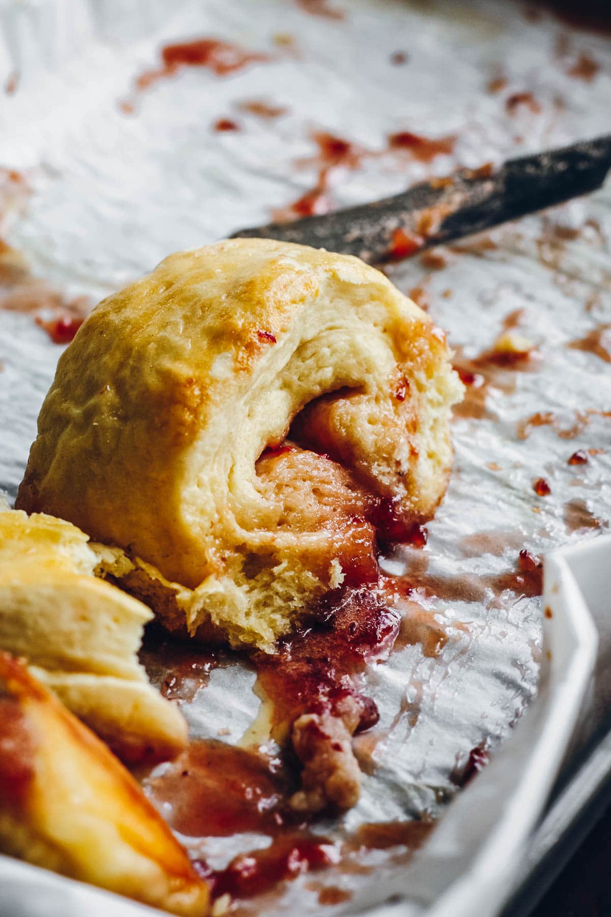 A sticky pinwheel jam scone on a tray with strawberry jam oozing out.