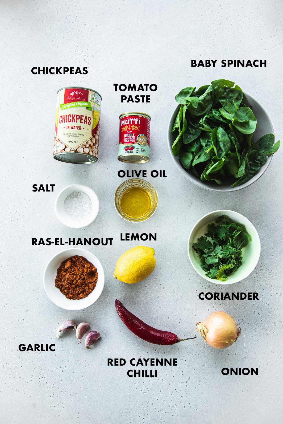 Ingredients for Spicy Moroccan Chickpeas labeled - chickpeas, tomato paste, spinach, garlic, chilli, onion, lemon, coriander, salt and ras-el-hanout.