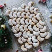 Kourabiedes - Greek Almond Crescent Cookies dusted with icing sugar on a wire rack surrounded by Christmas wreath and ornaments.