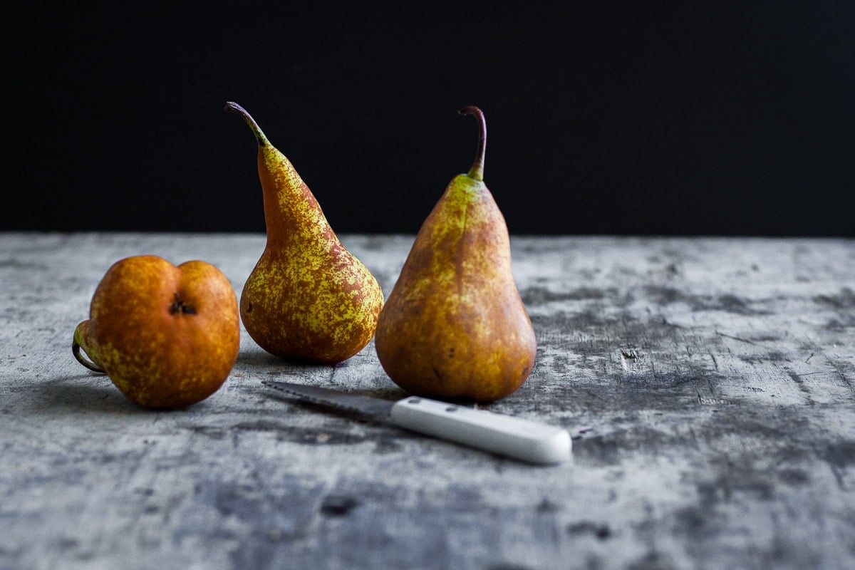 Three Beurre Bosc pears and a white paring knife resting on a table.