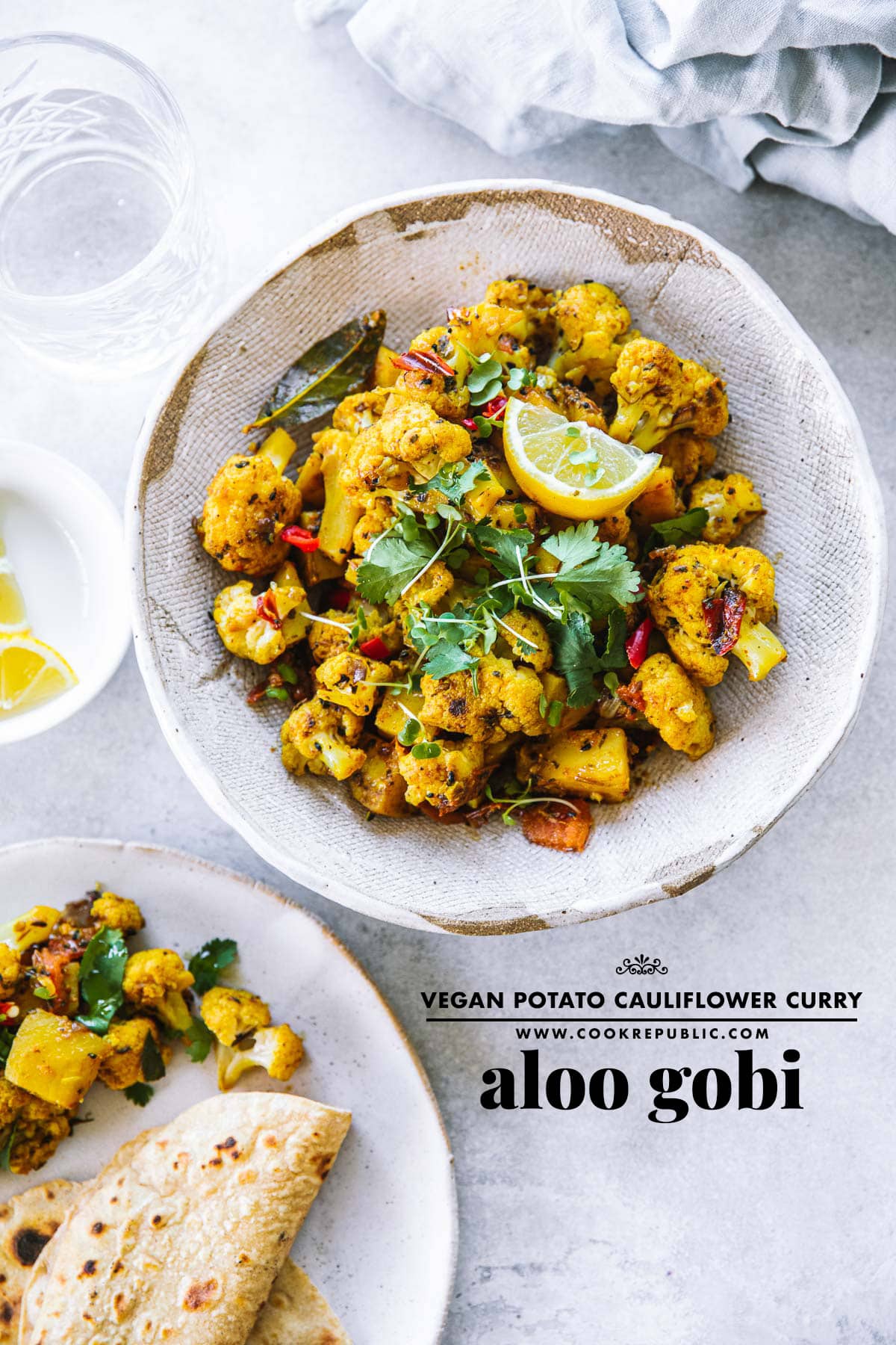 Aloo Gobi served in a bowl on a table with roti, lemon wedges and water.