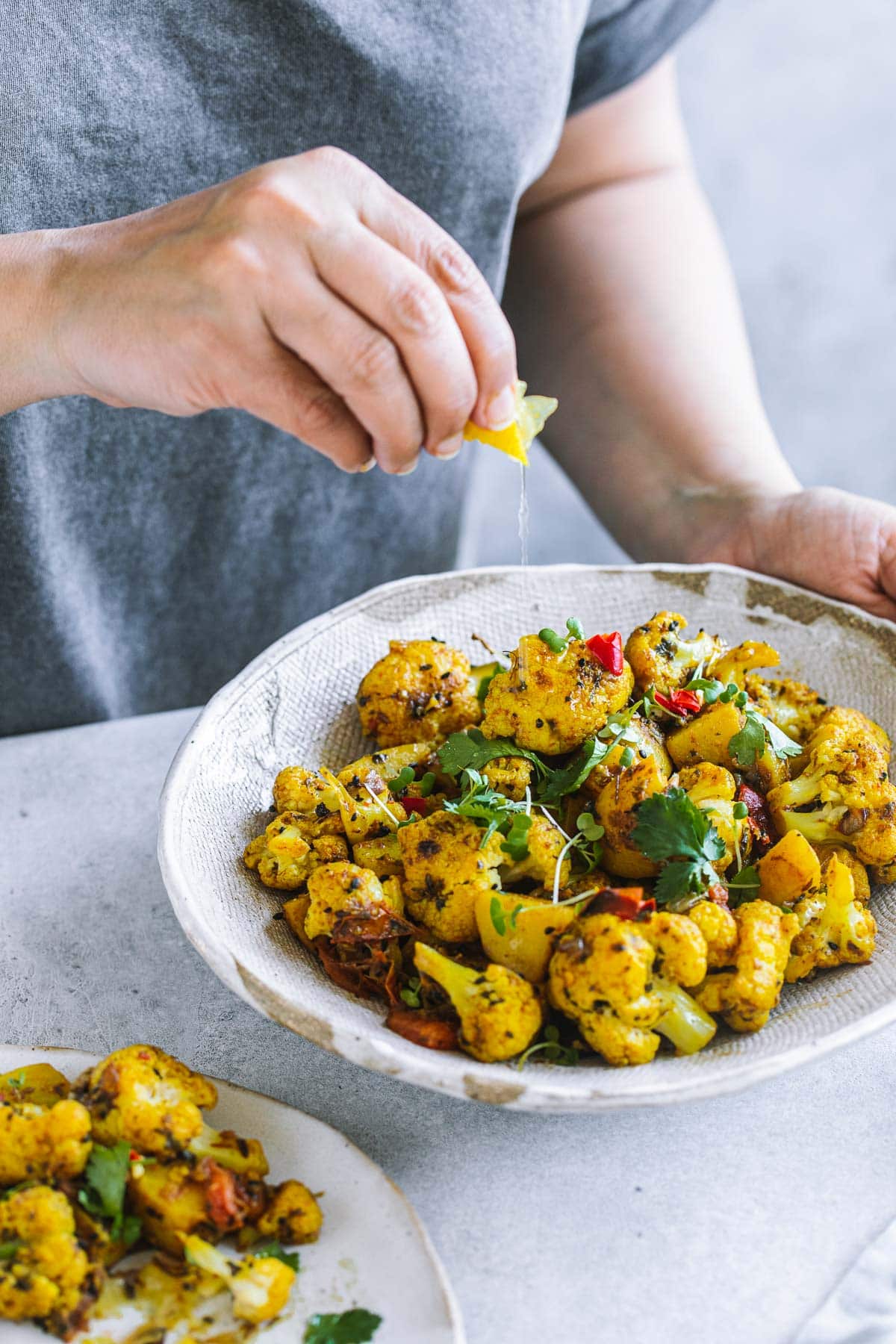 Squeezing lemon on aloo gobi served in a rustic bowl for dinner.