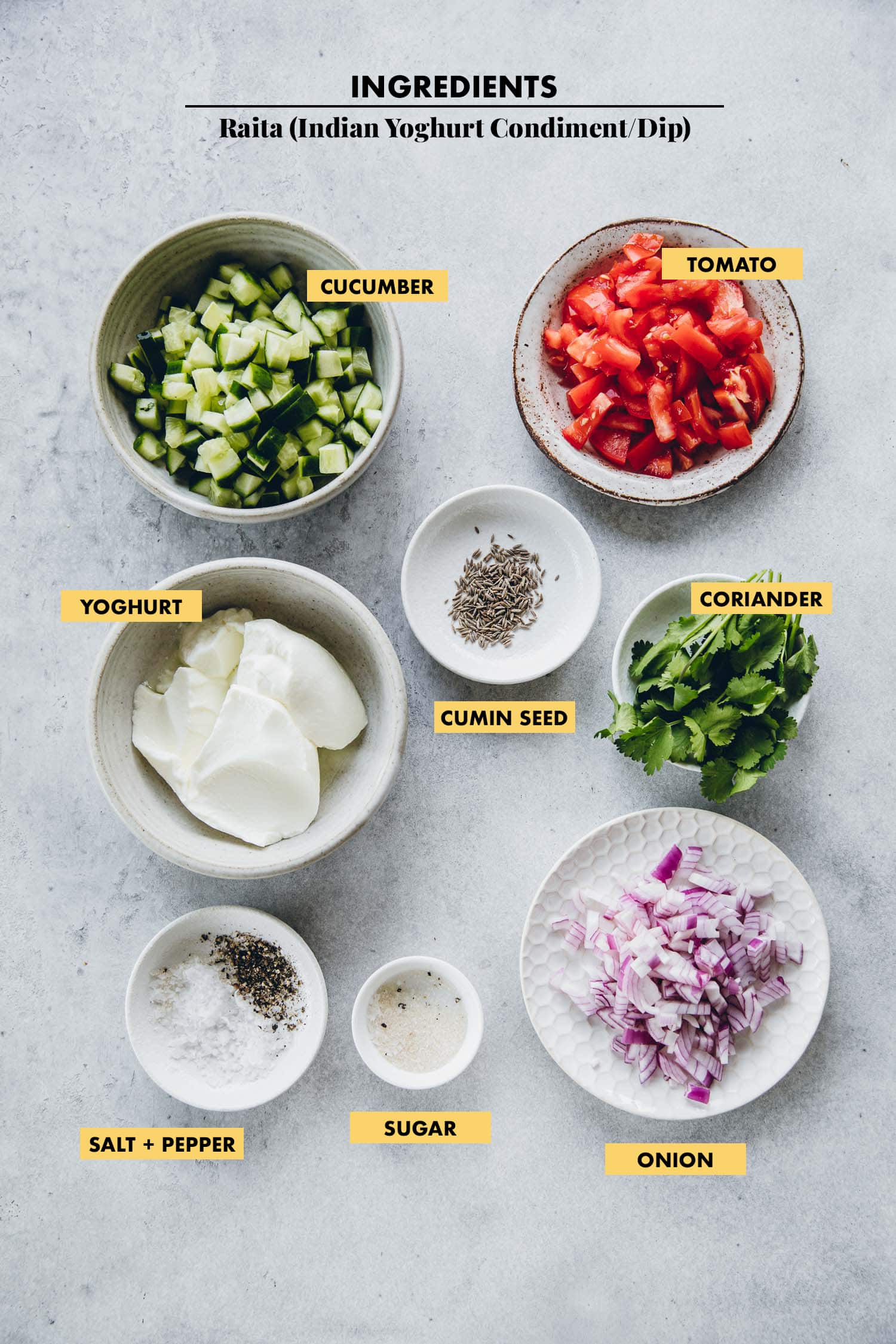 Ingredients for Indian Raita measured in bowls - cucumber, tomato, onion, coriander, yoghurt, salt, pepper, sugar and cumin.