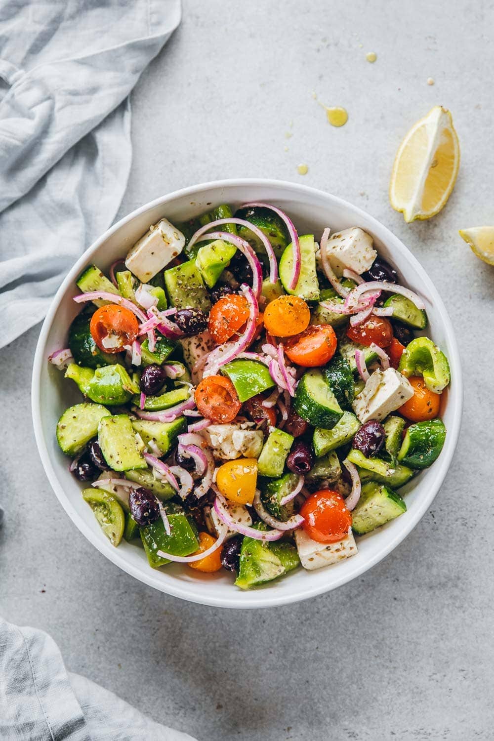 Classic Greek Salad in a white bowl on the table with lemon wedges on the side.