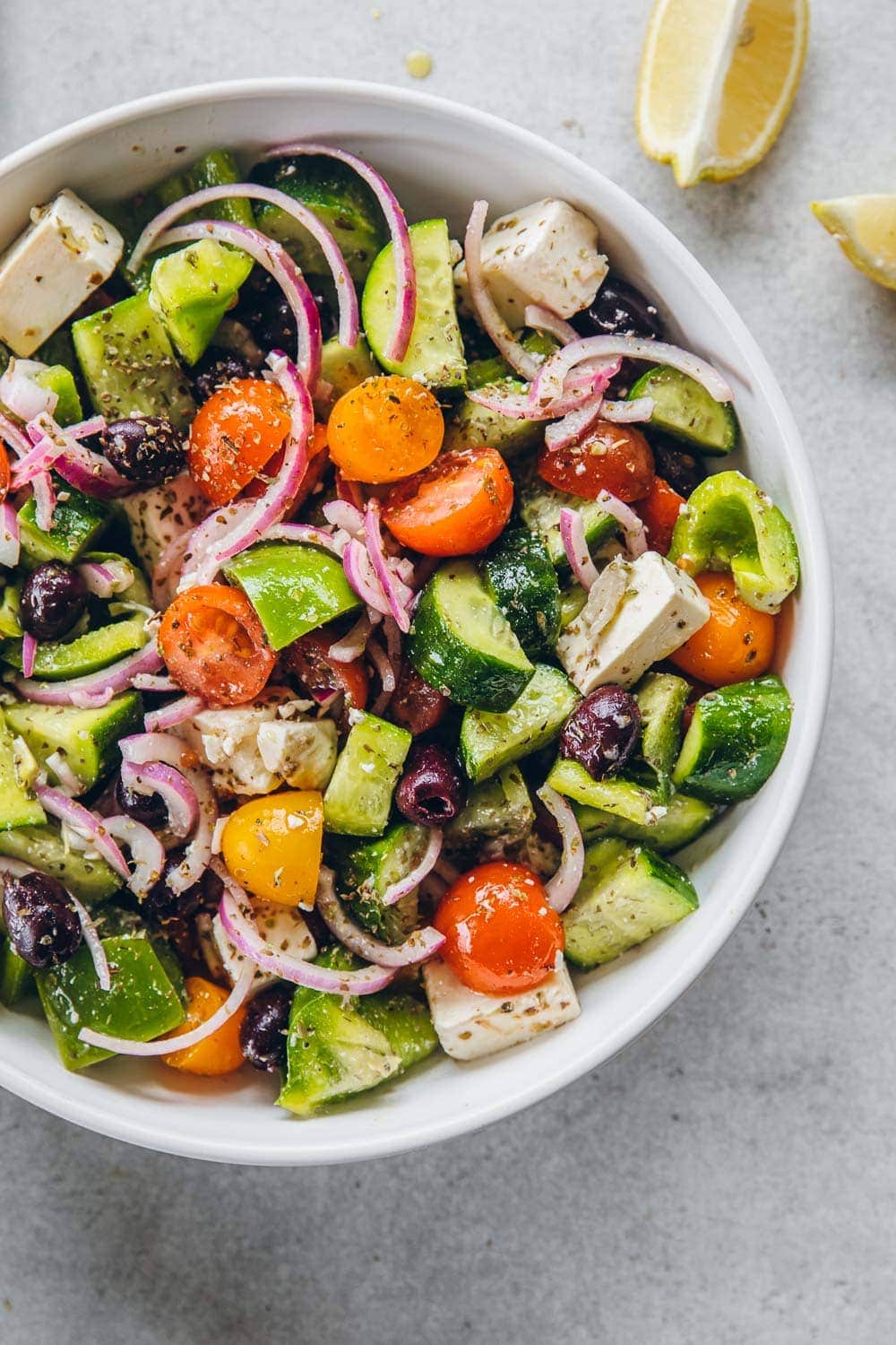 Chopped Greek salad veggies, feta cheese, olives and salad dressing in a bowl.