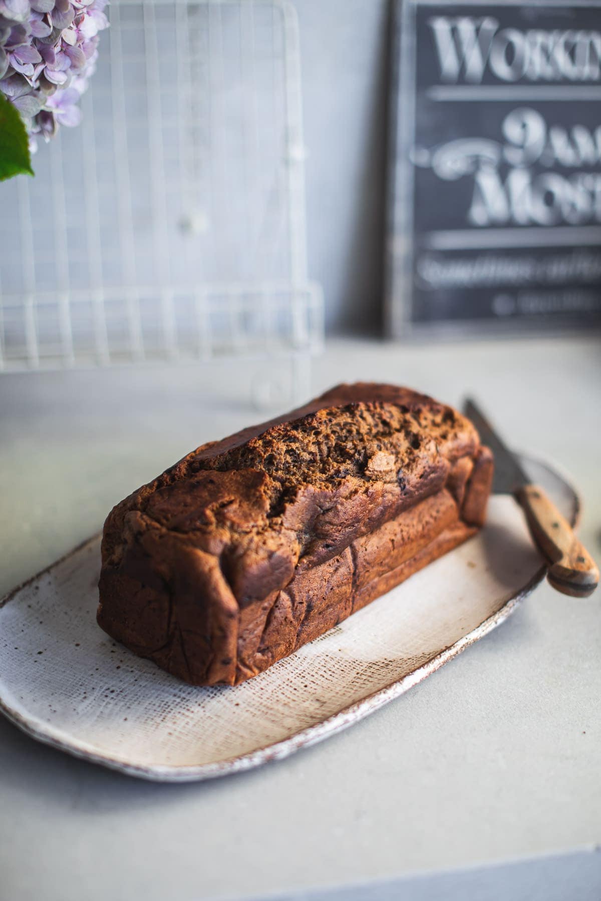 A loaf of baked Coffee Banana Bread on a plate with a knife resting next to it.
