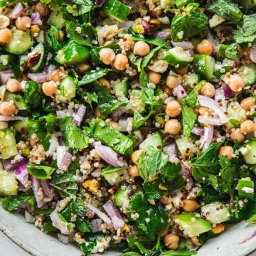 Close up of Jennifer Aniston Salad in a bowl - chickpea, quinoa, onion, cucumber, feta, pistachio and herbs tossed in dressing.