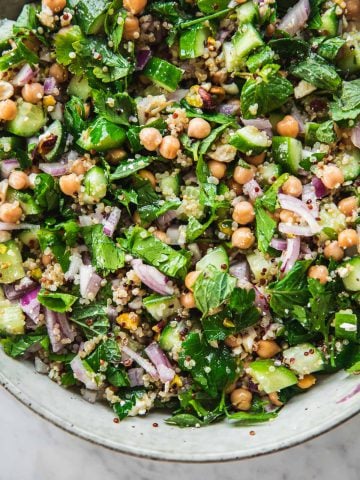 Close up of Jennifer Aniston Salad in a bowl - chickpea, quinoa, onion, cucumber, feta, pistachio and herbs tossed in dressing.