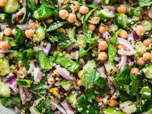 Close up of Jennifer Aniston Salad in a bowl - chickpea, quinoa, onion, cucumber, feta, pistachio and herbs tossed in dressing.