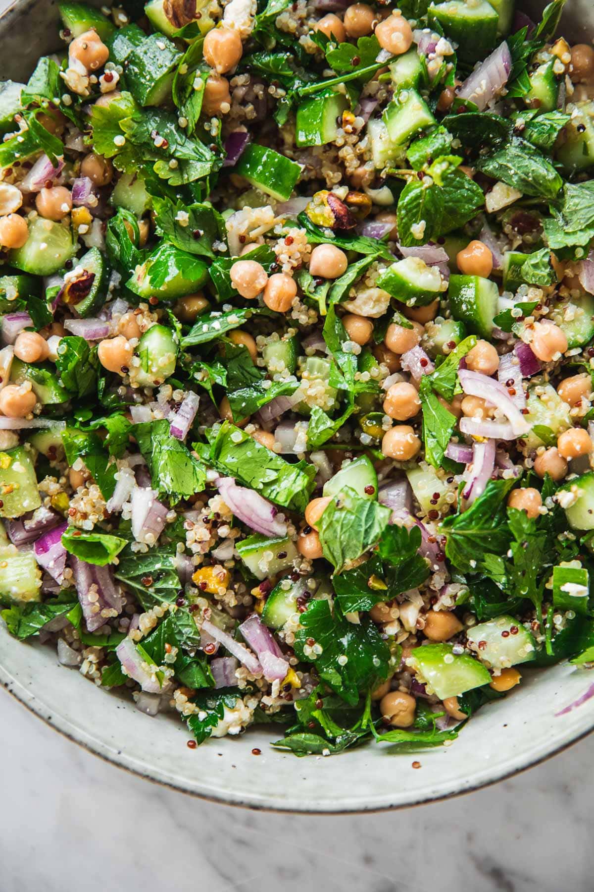 Close up of Jennifer Aniston Salad in a bowl - chickpea, quinoa, onion, cucumber, feta, pistachio and herbs tossed in dressing.