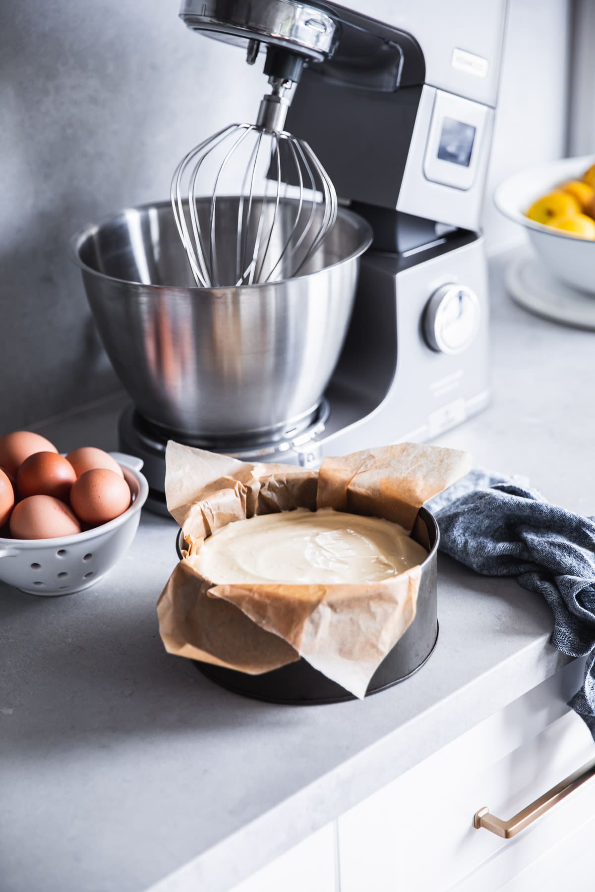 A stand mixer, bowl of eggs and cake tin filled with Basque Cheesecake batter on a kitchen counter