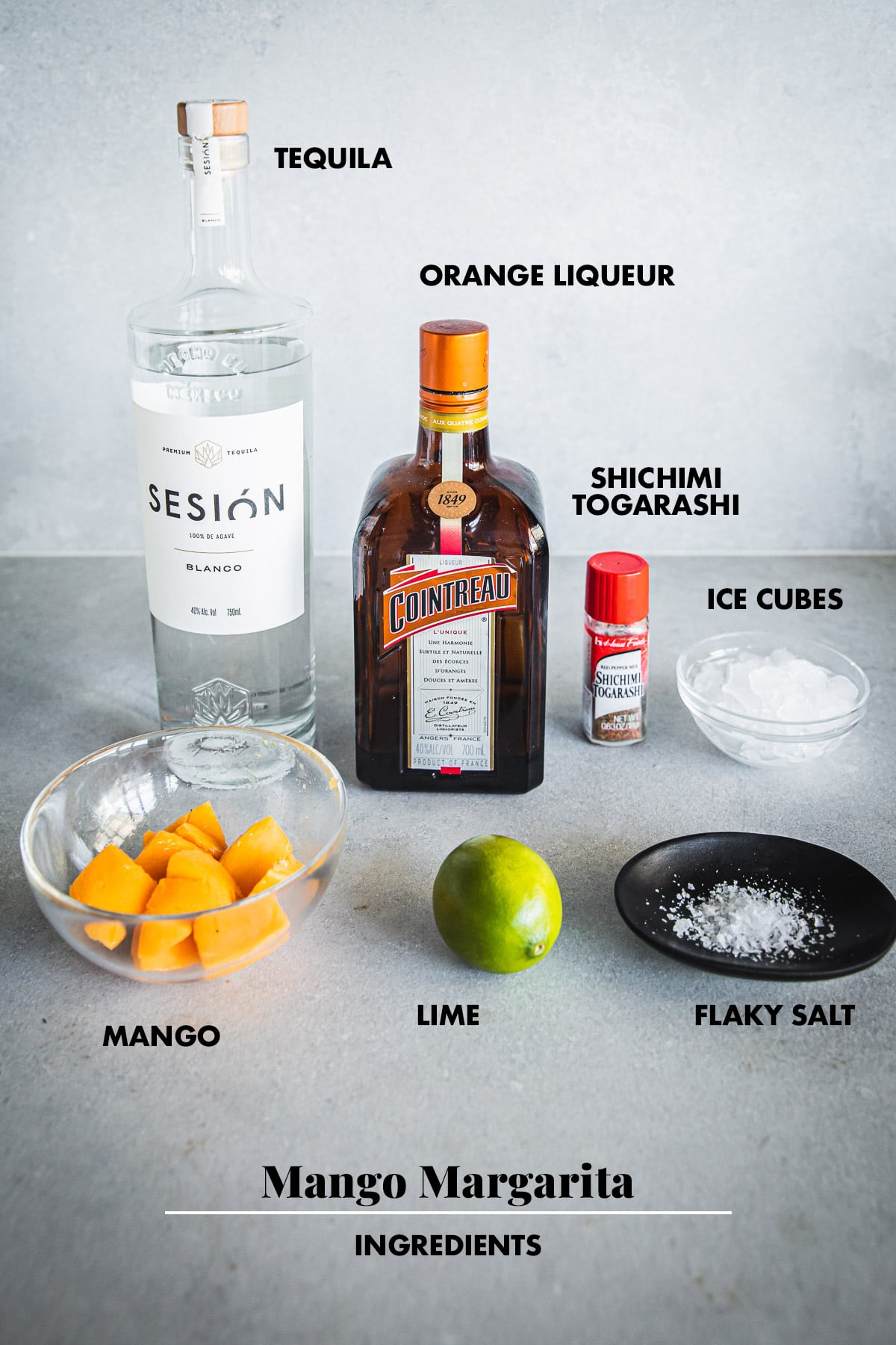 Mango margarita ingredients laid out and labeled - tequila, orange liqueur, Shichimi Togarashi, mango, lime, salt and ice.