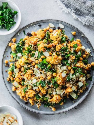 Roasted Cauliflower Salad With Chickpeas And Quinoa served in a salad platter with extra parsley and almond flakes on the side.