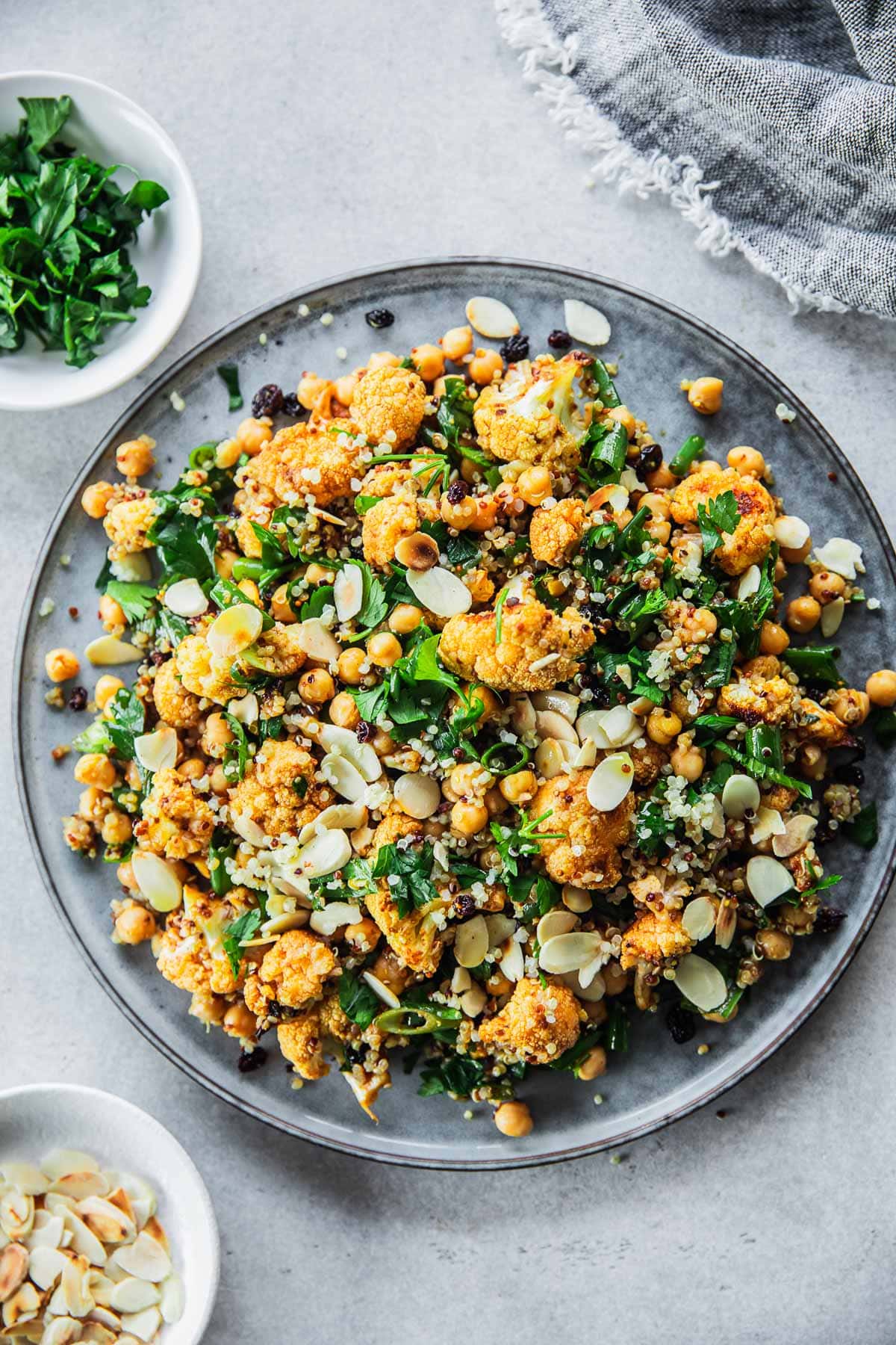 Roasted Cauliflower Salad With Chickpeas And Quinoa served in a salad platter with extra parsley and almond flakes on the side.