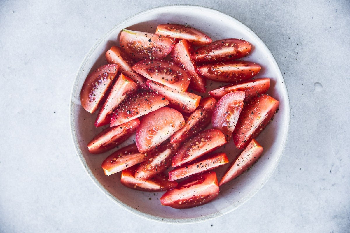 Tomatoes cut into wedges and sprinkled with salt and pepper in a bowl.