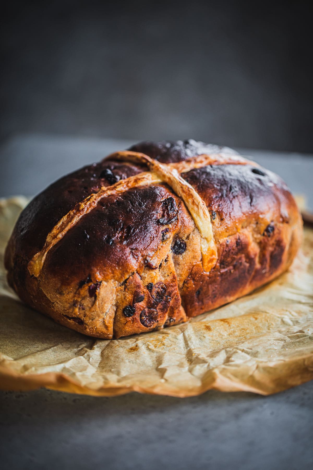 A baked Hot Cross Bun Loaf on top of baking paper on a table.