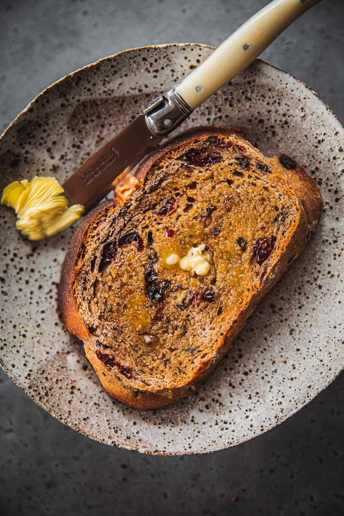 A toasted hot cross bun loaf slice on a plate with butter and butter knife.