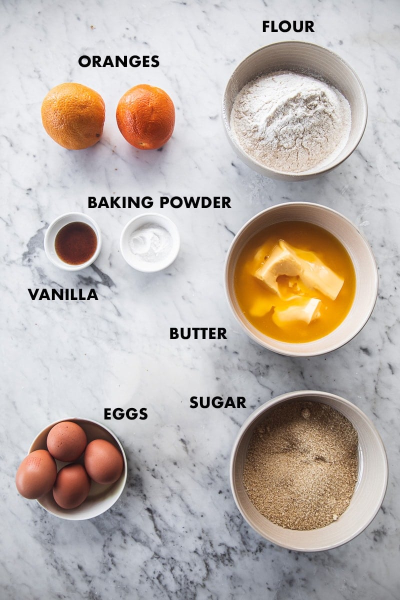 Ingredients for orange pound cake measured in bowls and labeled - flour, sugar, eggs, butter, oranges, vanilla and baking powder.