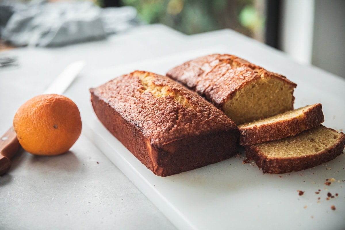 Loaves of orange pound cake resting on a chopping board on a table with an orange and bread knife to the side.