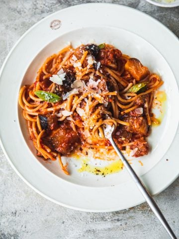 Pasta Alla Norma in a plate with a fork in the process of being eaten.