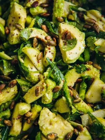 Green Avocado Salad tossed in a bowl with fresh slices of avocado, green apple, green bell pepper, herbs, toasted pepitas and salad dressing.