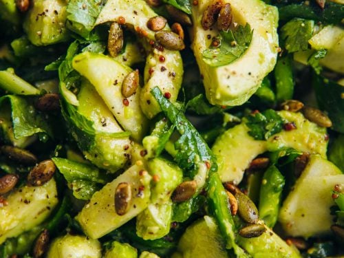 Green Avocado Salad tossed in a bowl with fresh slices of avocado, green apple, green bell pepper, herbs, toasted pepitas and salad dressing.