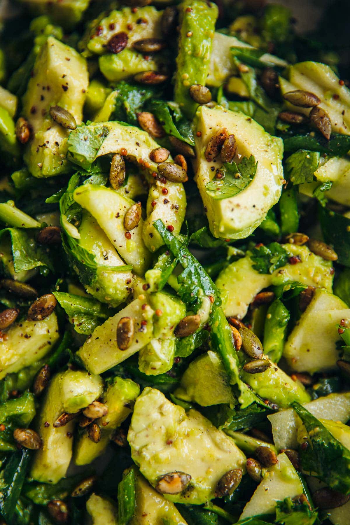 Green Avocado Salad tossed in a bowl with fresh slices of avocado, green apple, green bell pepper, herbs, toasted pepitas and salad dressing.