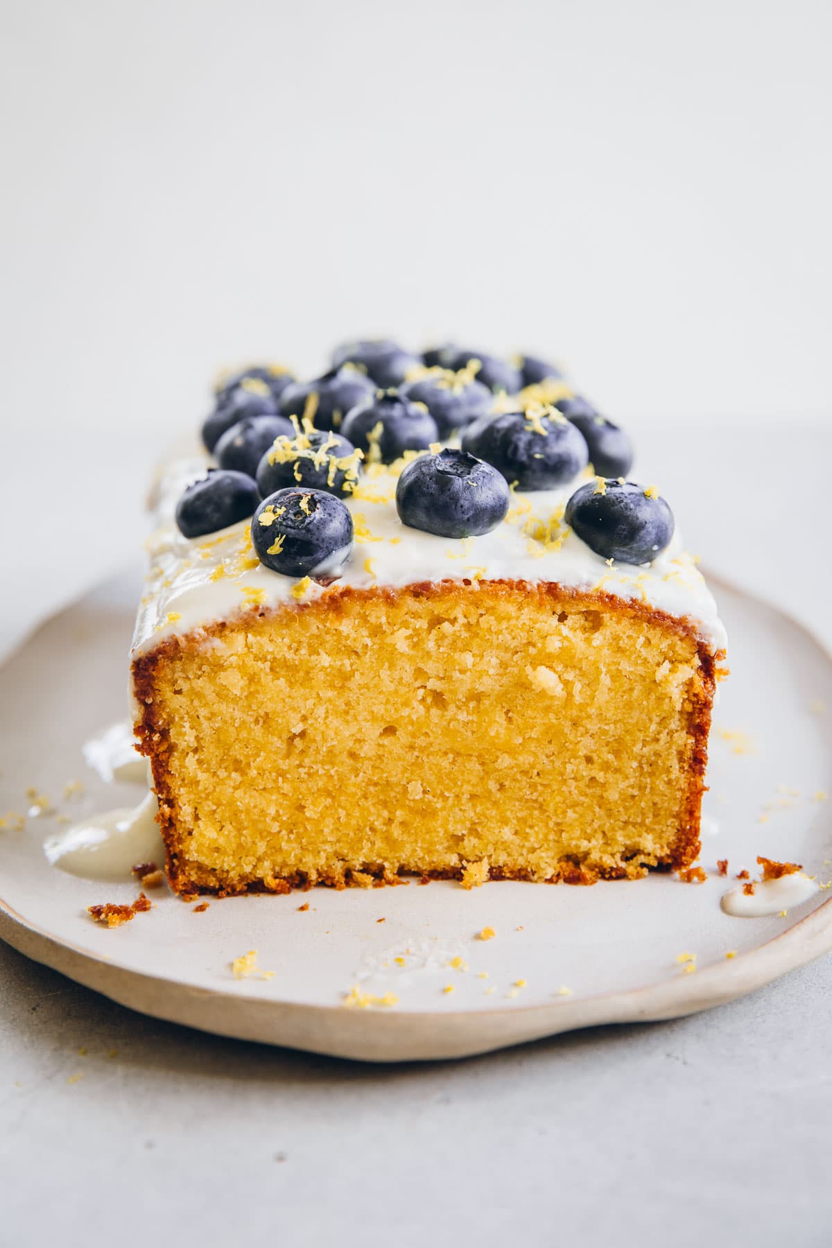 Blueberry Lemon Loaf Cake With Yoghurt Icing and fresh blueberries cut to reveal the yellow crumb.