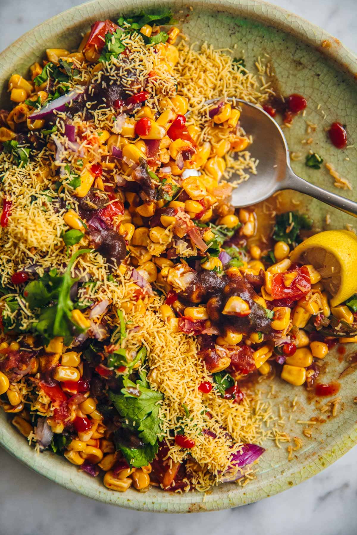 Corn Chaat (Corn Masala) served in a green plate with a spoon.