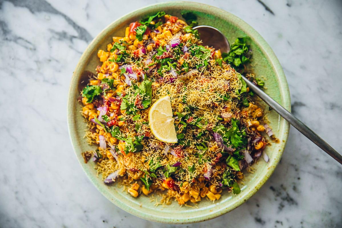 Corn Chaat serving in a green plate with a lemon wedge on top.