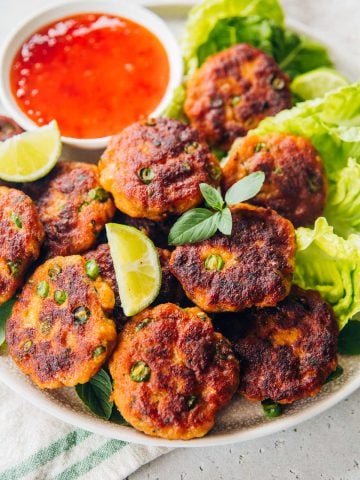 Thai Fish Cakes served on a platter with sweet chilli sauce, lime wedges and Cos lettuce.