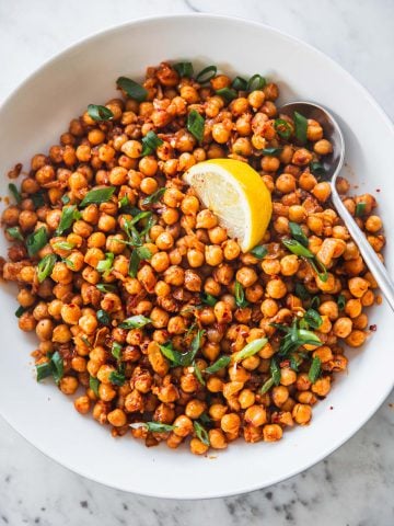 Sauteed Spicy Chickpeas in a white bowl with a lemon wedge and spoon.