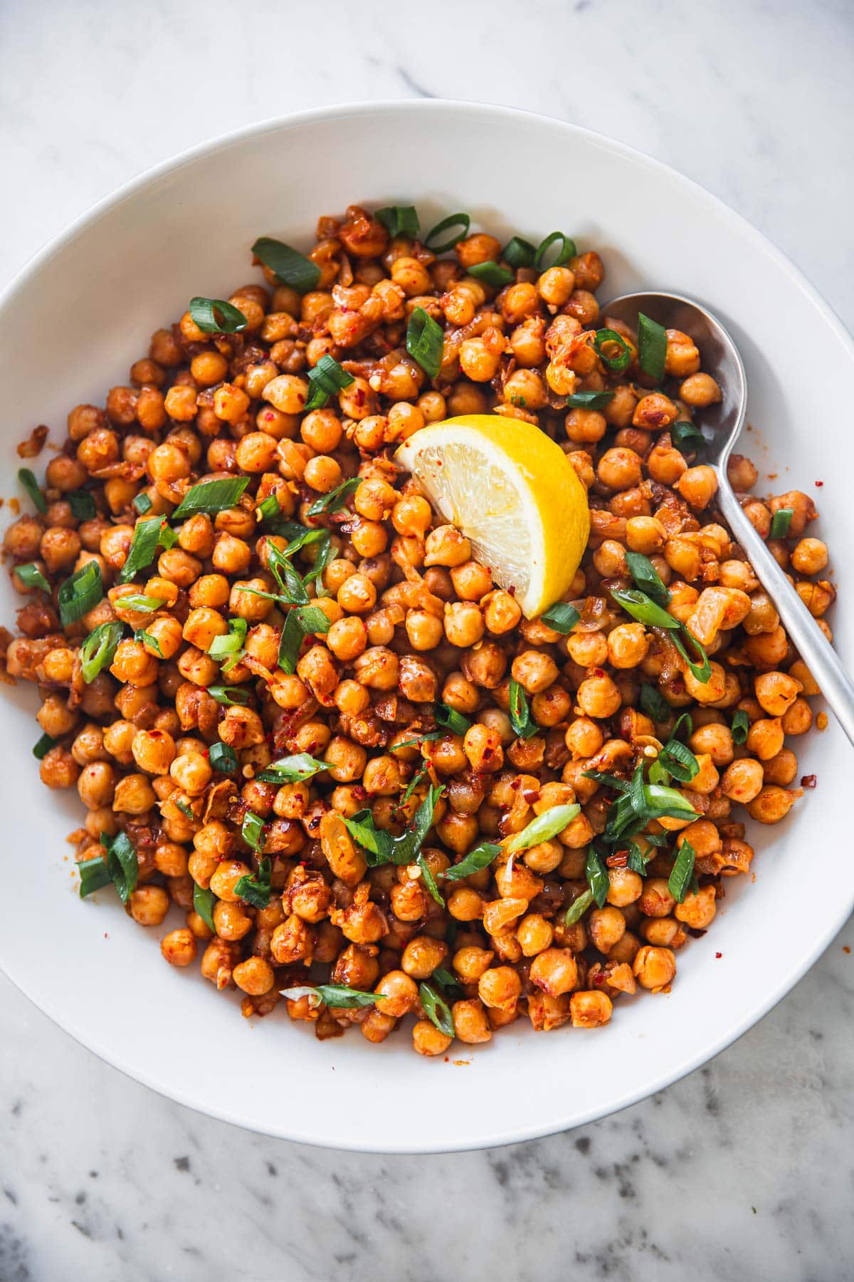 Sauteed Spicy Chickpeas in a white bowl with a lemon wedge and spoon.