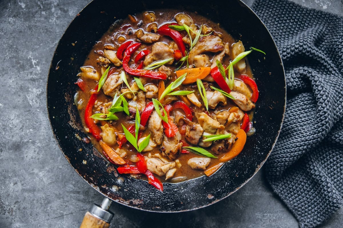 Chinese Satay Chicken stir fry in a wok with a dark grey napkin on a table.