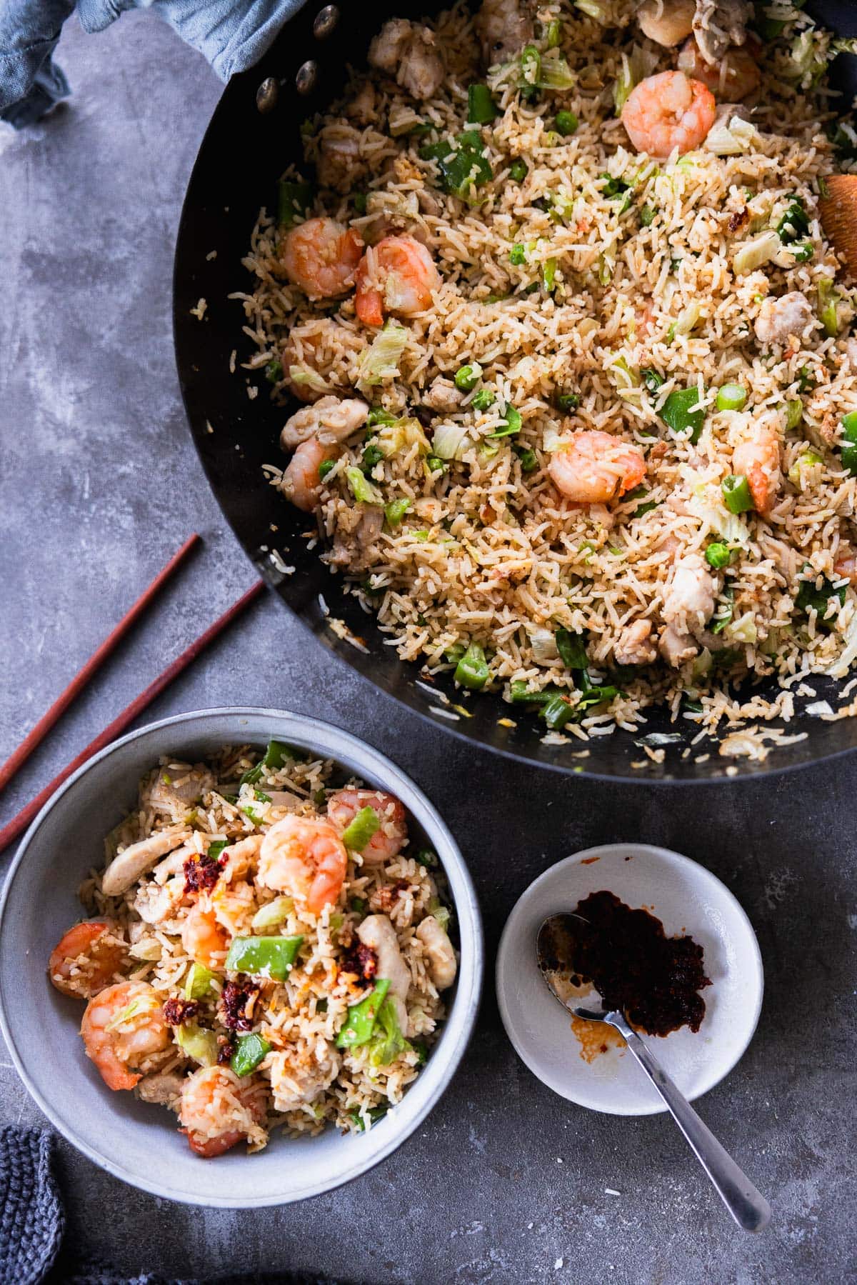 Shrimp And Chicken Fried Rice served in a bowl with chilli oil on the side. On a table with a wok full of fried rice and chopsticks.