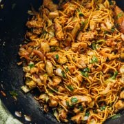 Chicken Schezwan Noodles in a wok with a green tea towel wrapped around the wooden handle.
