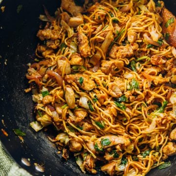 Chicken Schezwan Noodles in a wok with a green tea towel wrapped around the wooden handle.
