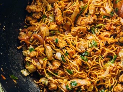 Chicken Schezwan Noodles in a wok with a green tea towel wrapped around the wooden handle.