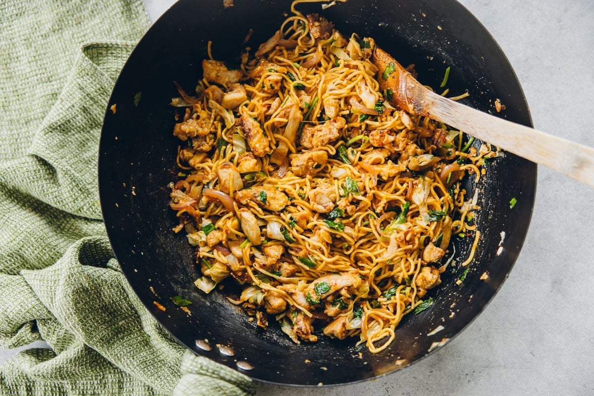 Chicken Schezwan Noodles in a wok with a green tea towel.