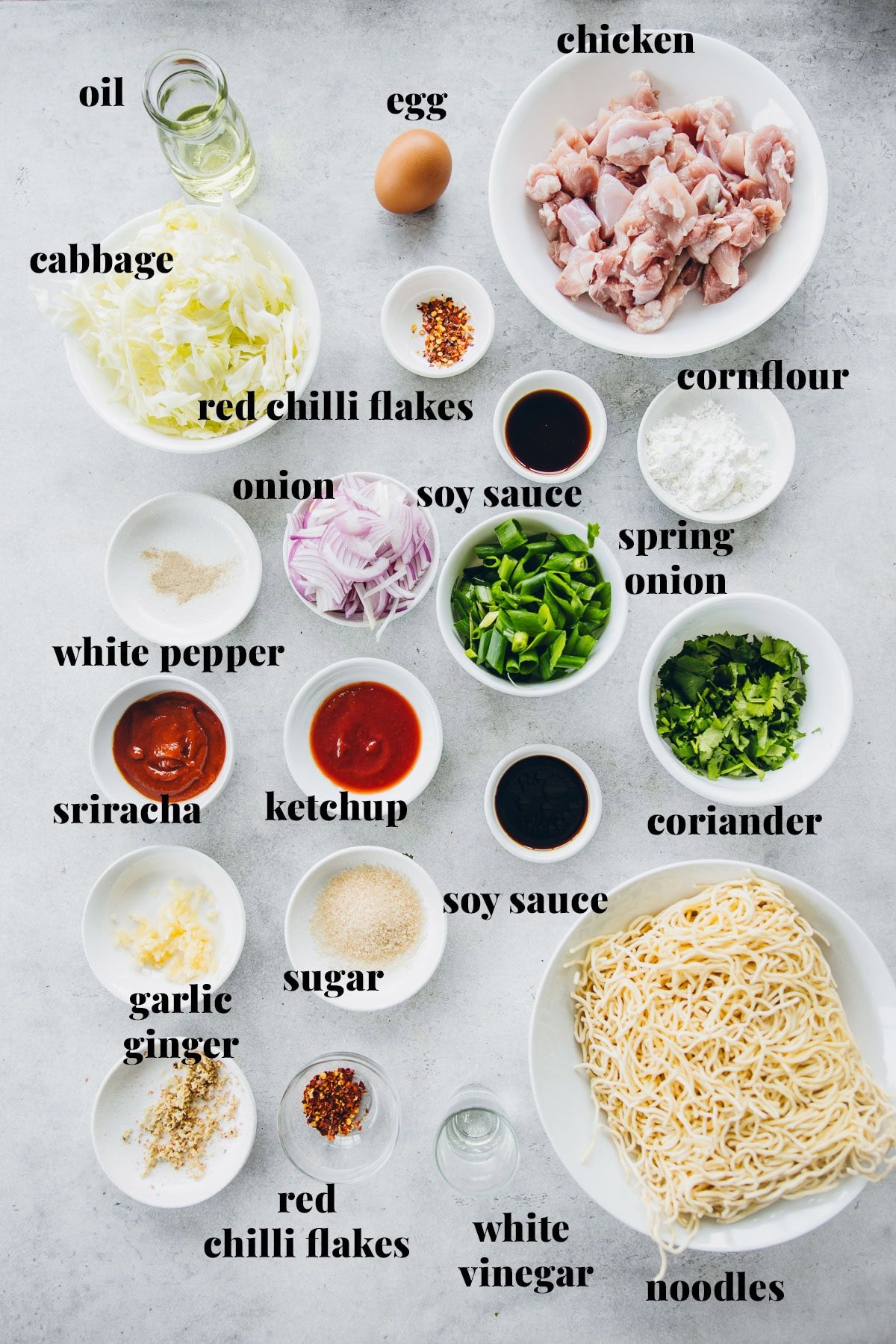Chicken Schezwan Noodle Ingredients measured and labeled - Chicken, chow mein noodles, onion, cabbage, spring onion, garlic, ginger, chilli flakes, tomato ketchup, Sriracha, white vinegar, soy sauce, cornstarch, egg, coriander, salt and pepper.
