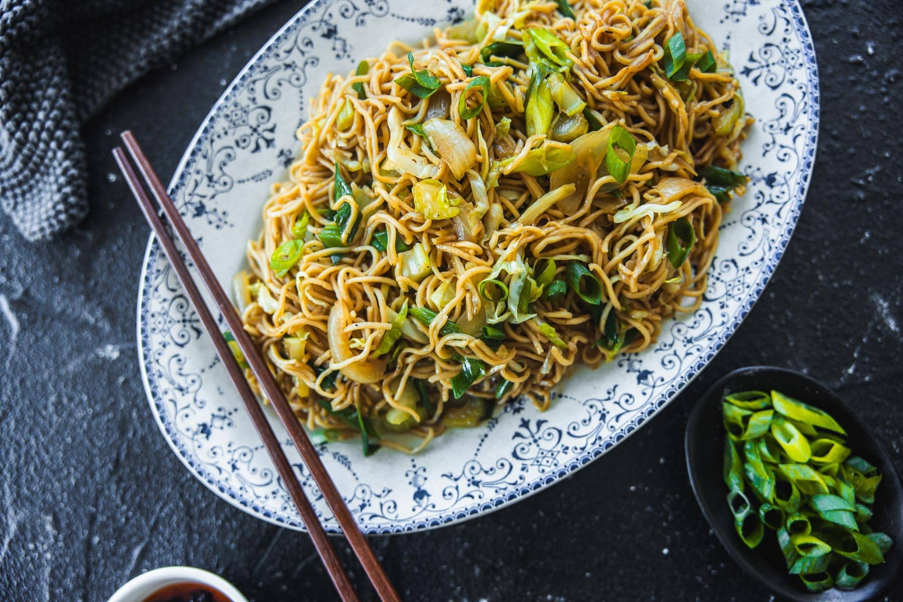 Panda Express Chow Mein Noodles served in an oval platter with chopsticks, napkin and extra spring onion on the side.